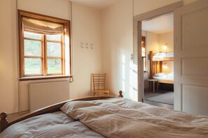 Un dormitorio con una cama, una ventana con cortinas, una silla y una puerta que da a otra habitación.