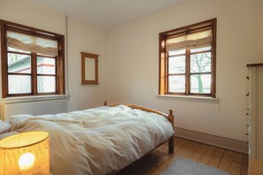 Un dormitorio con una cama de madera, dos ventanas con cortinas, una lámpara de noche y un espejo en la pared.