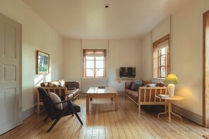 Una sala de estar con piso de madera, un sofá, una silla, una mesa de centro y un televisor.