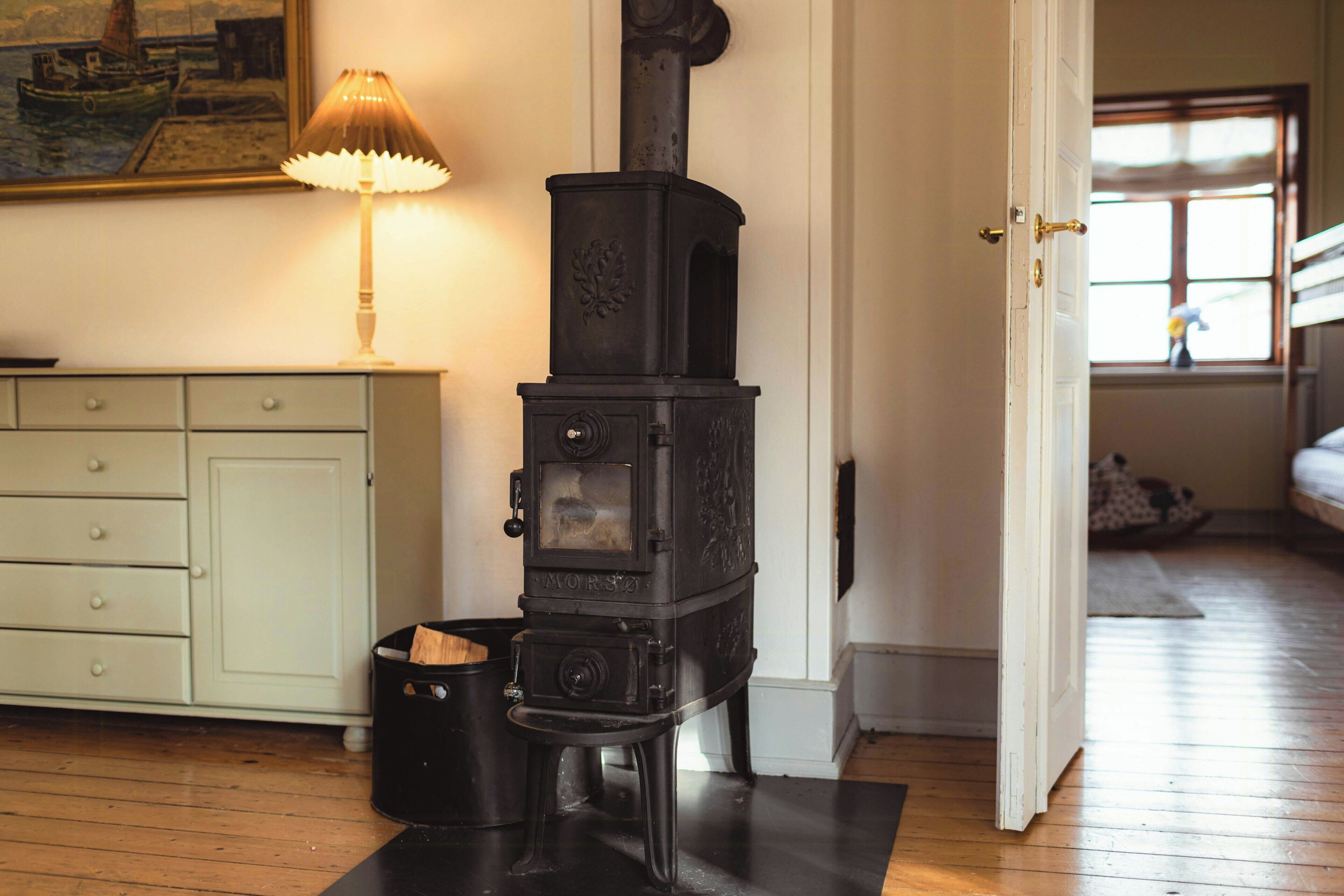 A room with a black stove, a lamp, a cabinet, and a door leading to another room.