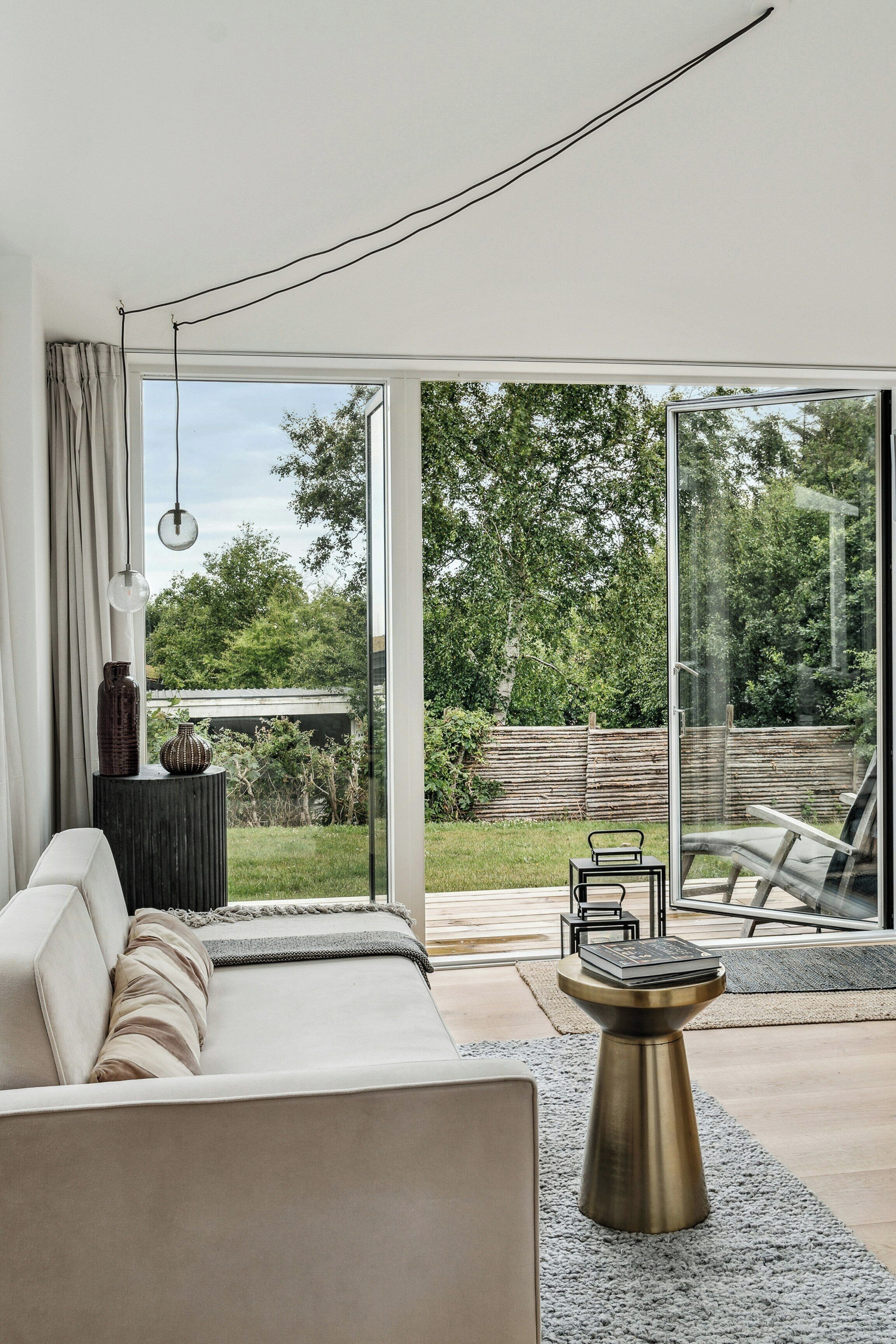 A modern living room with a sofa, a coffee table, and a view of a garden through large glass doors.