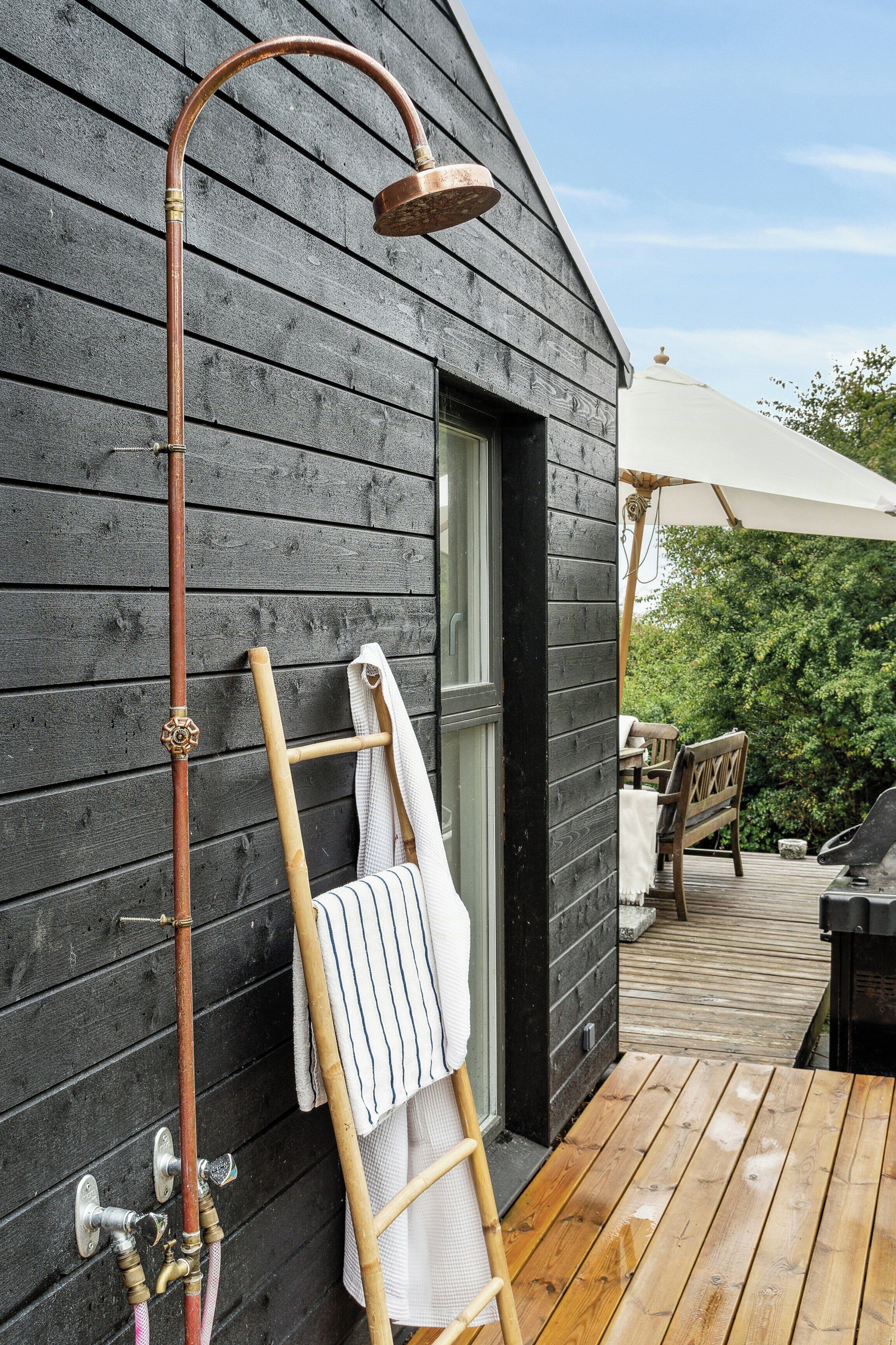 Une terrasse en bois avec une pomme de douche en métal, une serviette sur un porte-serviettes et un banc en bois.