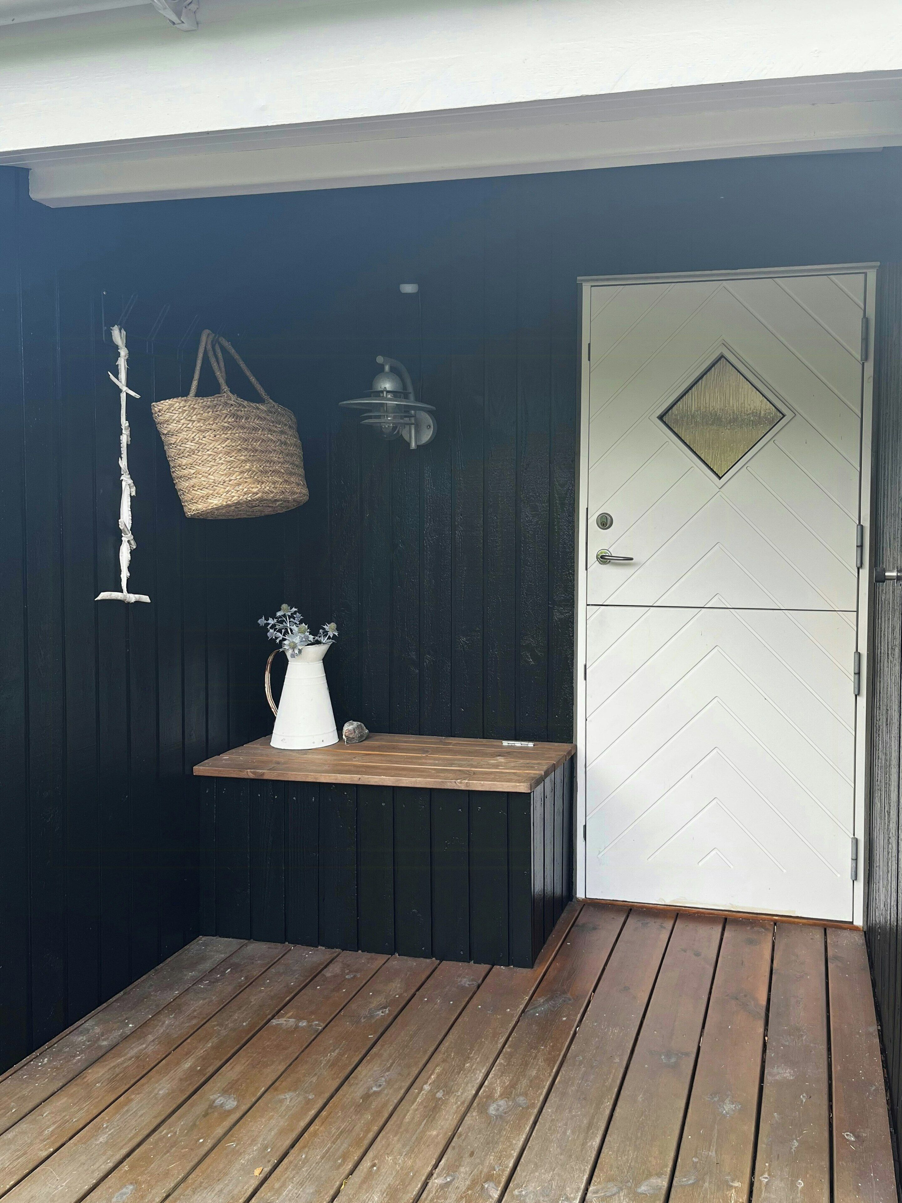 A wooden deck with a white door and a small table with a vase and basket.