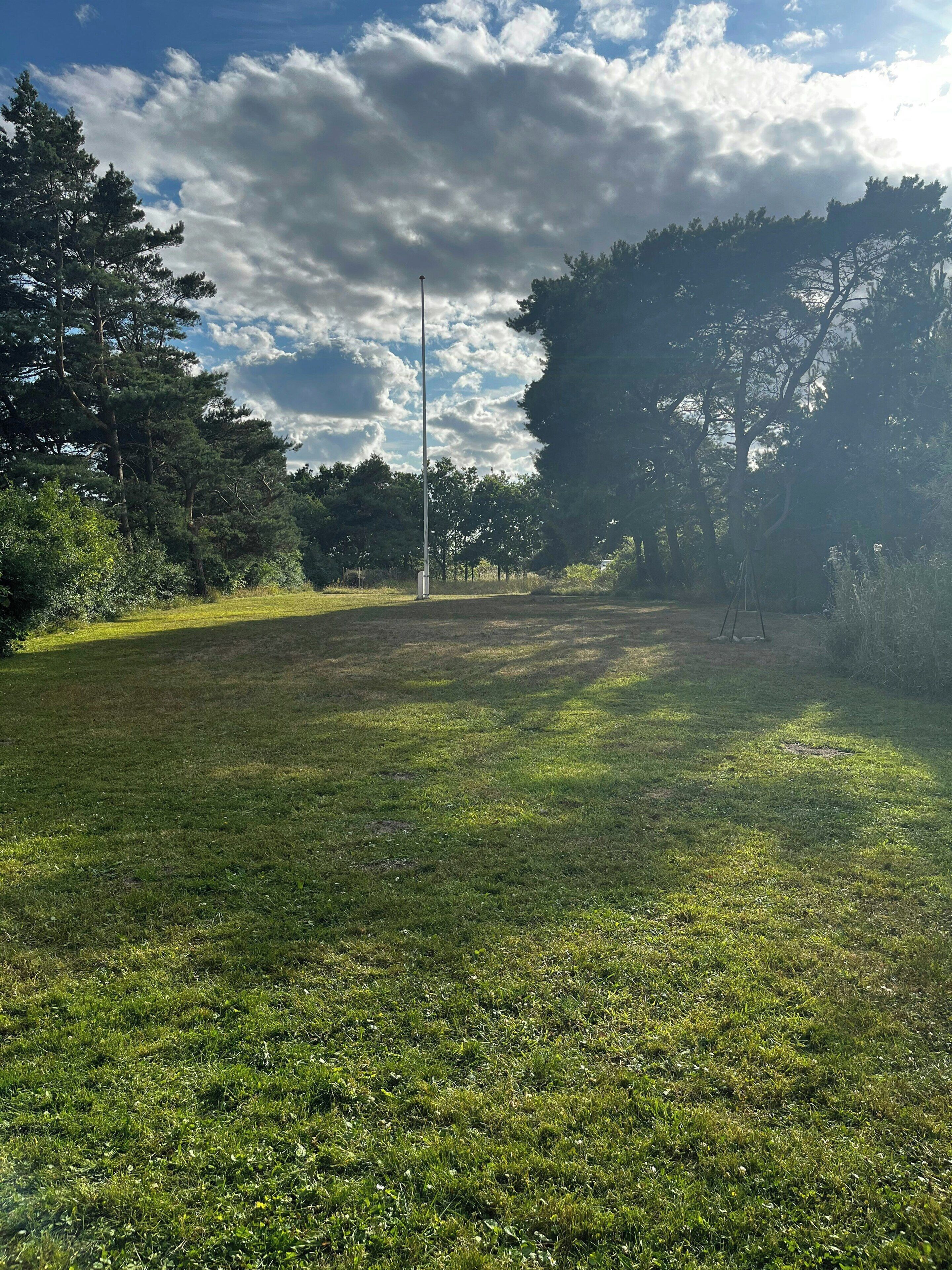 Een grasveld met een hoge paal, bomen en een heldere lucht.