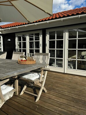 Eine Holzterrasse im Freien mit Tisch und Stühlen, einem Korbwäscher mit Essen und einem großen Sonnenschirm.