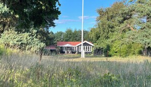 Ein Haus mit rotem Dach und weißer Fassade, umgeben von hohem Gras und Bäumen.
