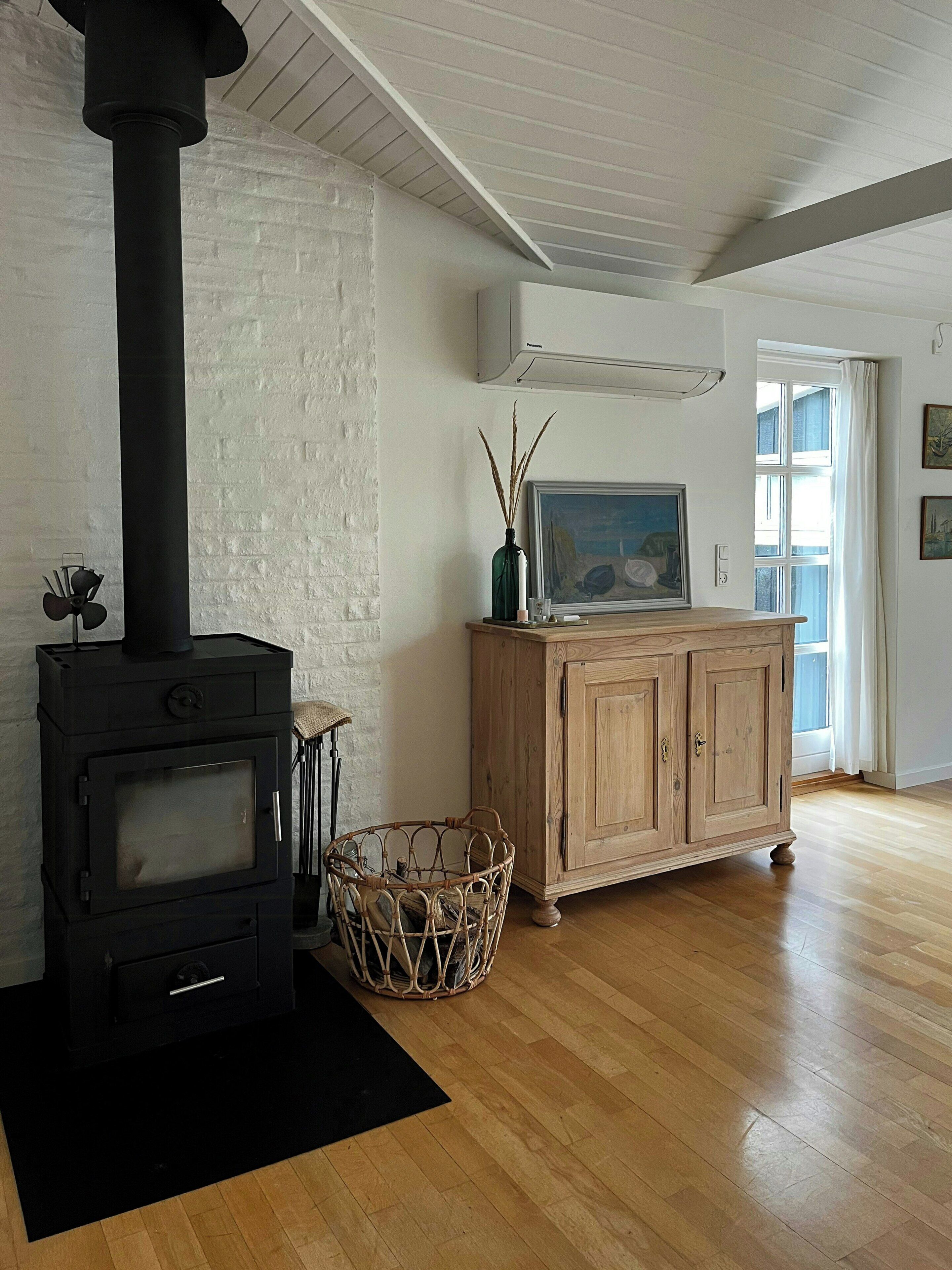 A room with a black wood-burning stove, a wicker basket, a wooden cabinet, and a painting on the wall.