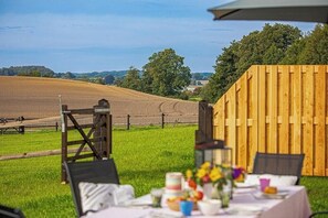 Ein Essbereich im Freien mit einem Tisch für zwei Personen, einem Holzzaun und Blick auf ein Feld.
