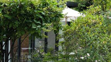 A garden with various plants and flowers, a tree, and a building with a white roof.