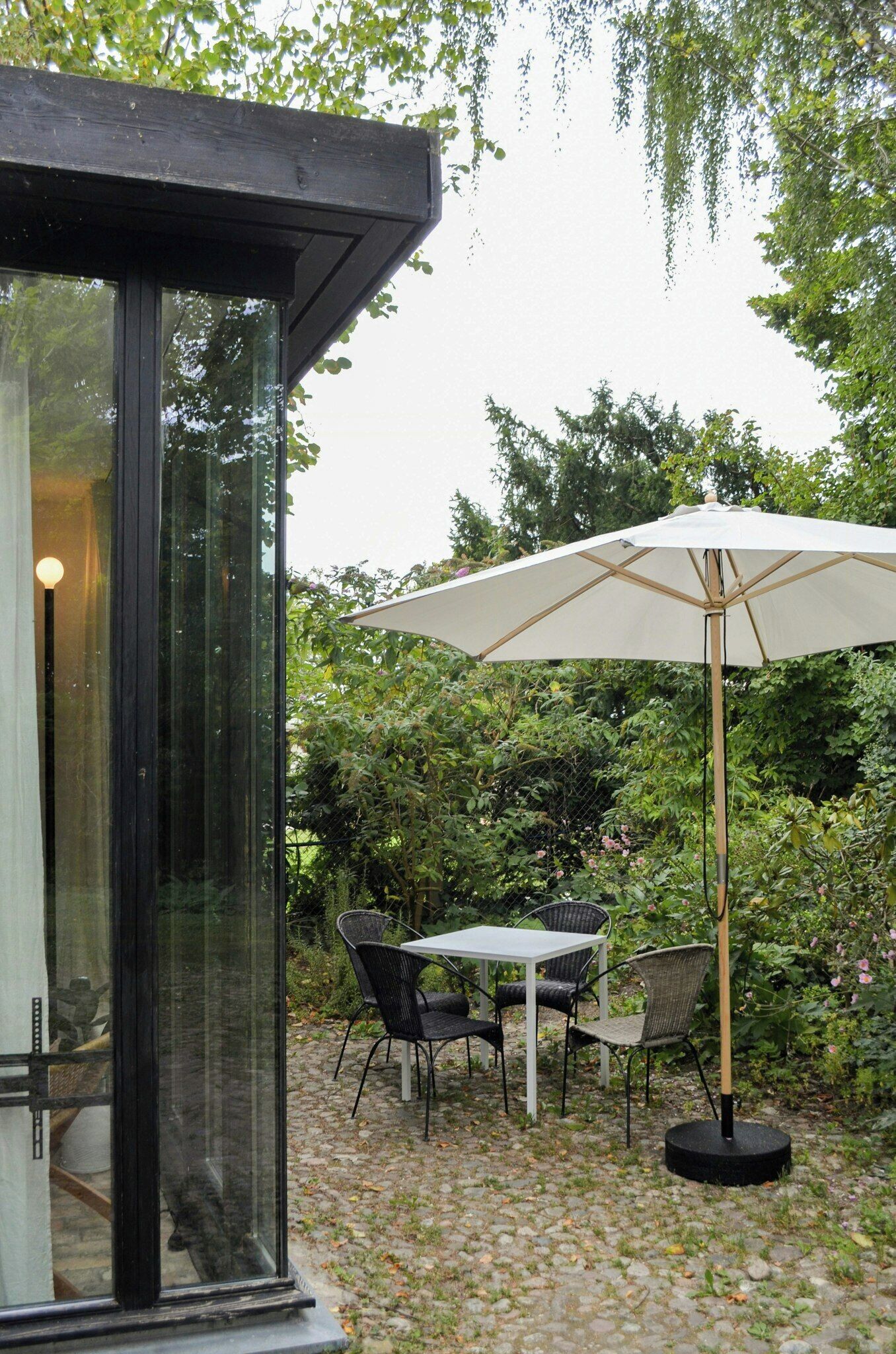 A glass-enclosed patio with a table and chairs, an umbrella, and lush greenery in the background.