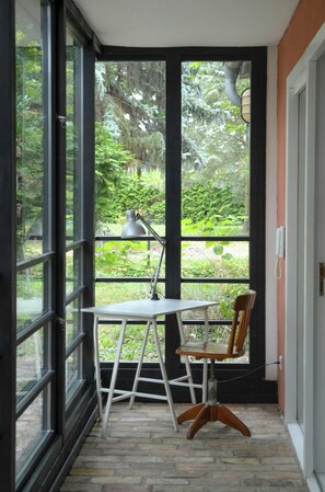 Ein Zimmer mit Tisch und Stuhl, großen Fenstern und Blick auf Grünfläche.