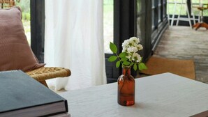 A room with a table, a book, a vase with flowers, a wicker chair, and a view through large windows. - Inspiring holiday home on the Havel (Werder (Havel))