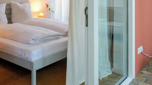 A bedroom with a bed, a nightstand with a lamp, and a sliding glass door leading to a balcony. - Inspiring holiday home on the Havel (Werder (Havel))