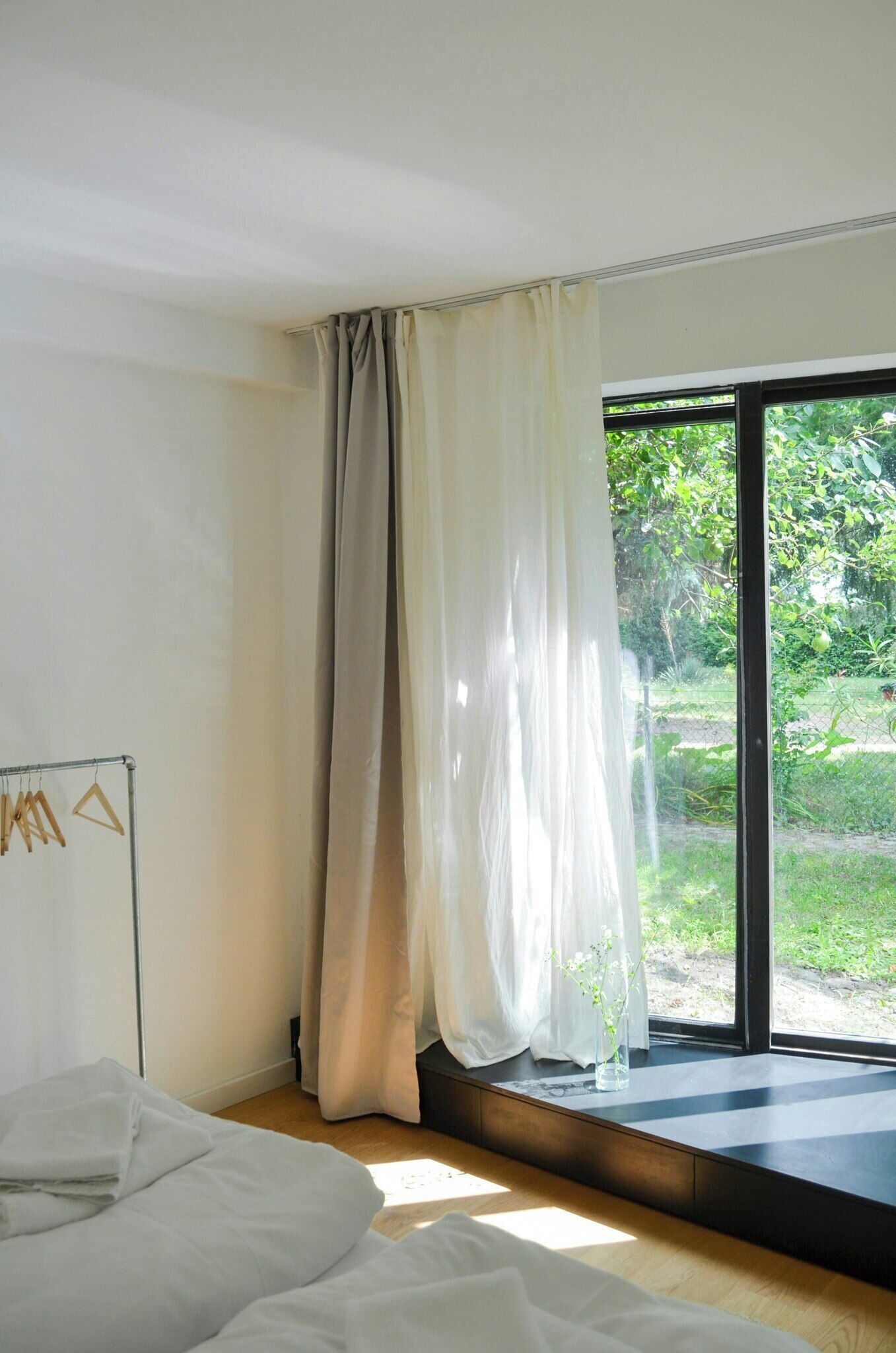 Ein Schlafzimmer mit einem Bett, einem Fenster mit Vorhängen und Blick auf Grünfläche.