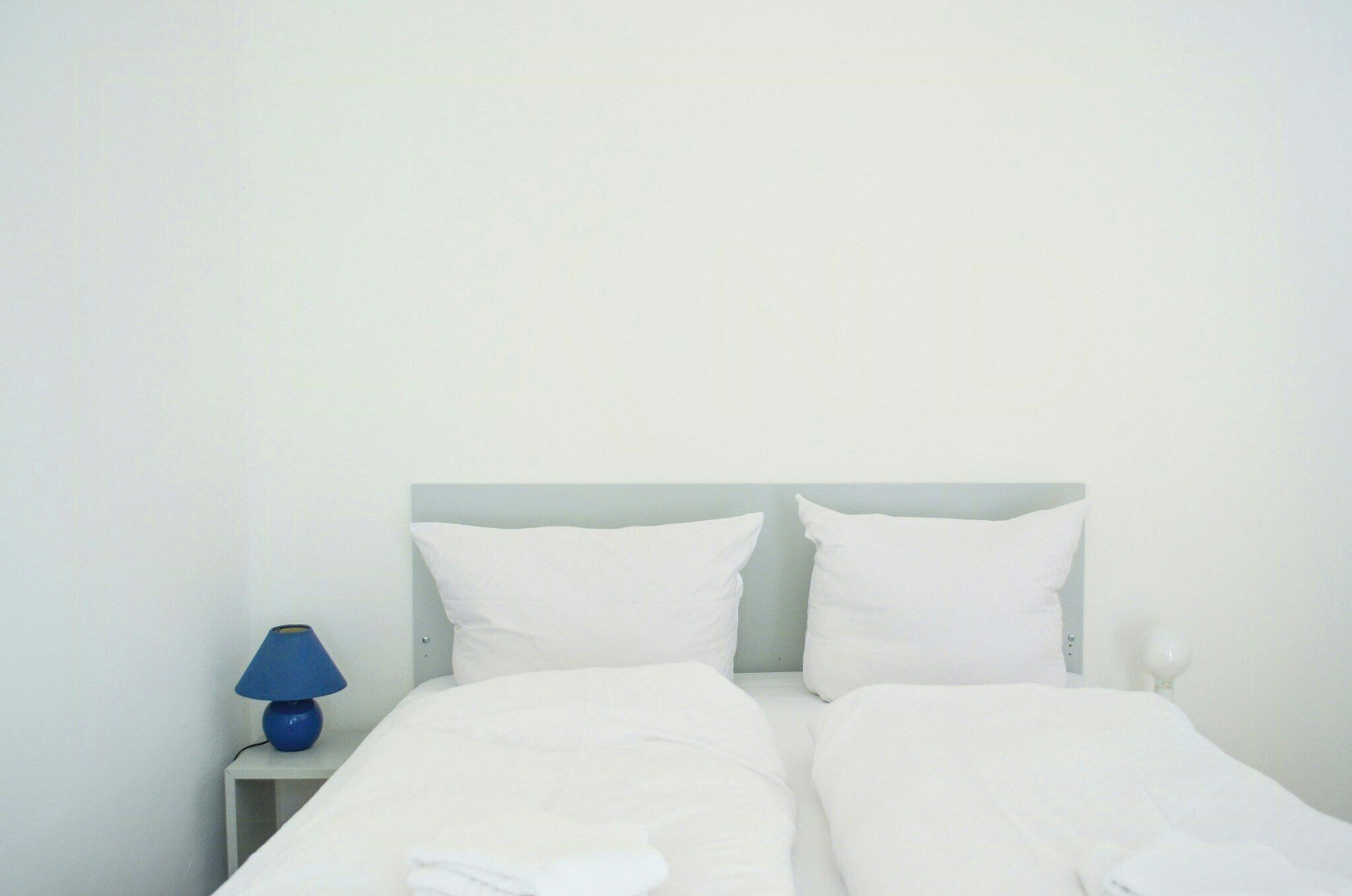 A bed with white bedding, a blue lamp, and a white nightstand.