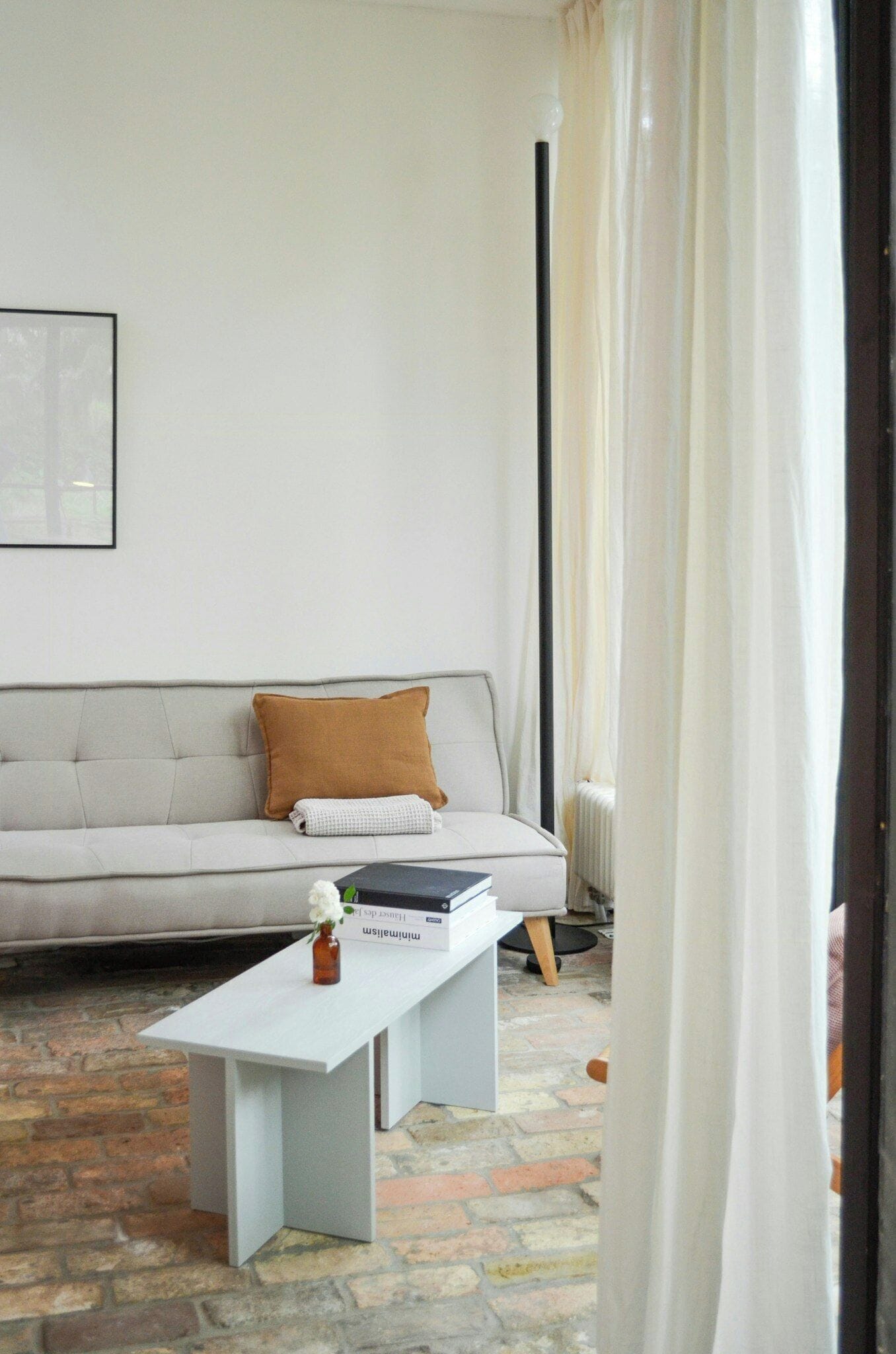 A living room with a sofa, a white coffee table, and a small vase with flowers.