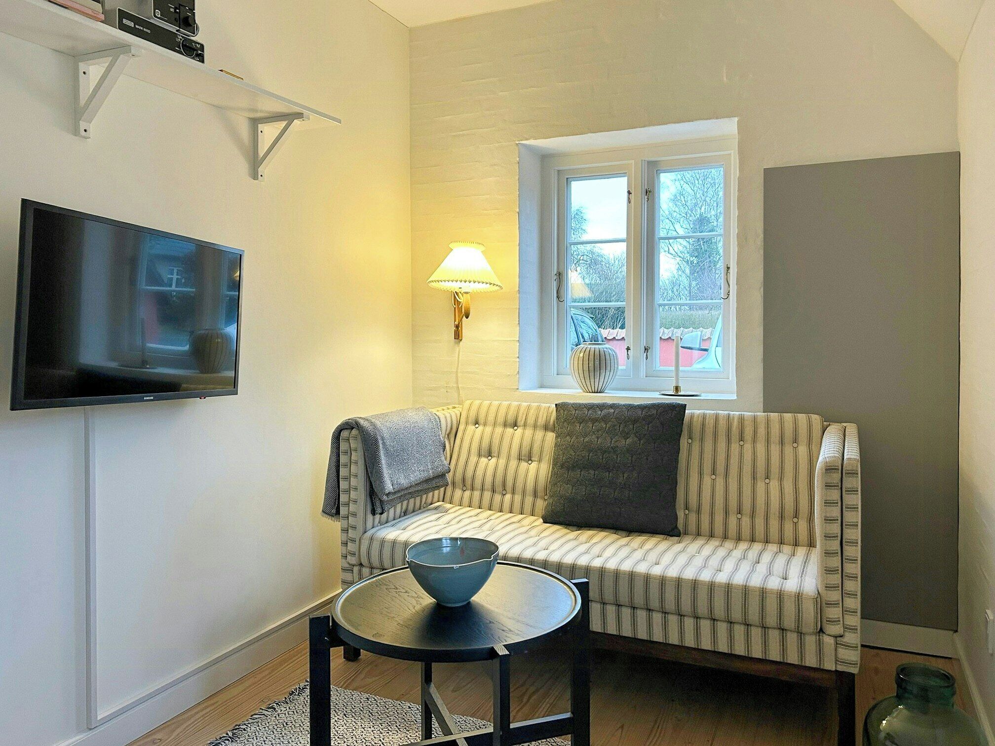 Una sala de estar con un sofá, un televisor, una lámpara y una ventana.