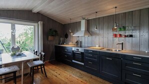 A modern kitchen with wooden flooring, a dining area with a table and chairs, and a large window. - Cozy private holiday home on Lifjell (Bø)