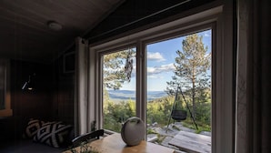 A room with a large window overlooking a forested landscape, a wooden table with a vase, and a chair. - Cozy private holiday home on Lifjell (Bø)