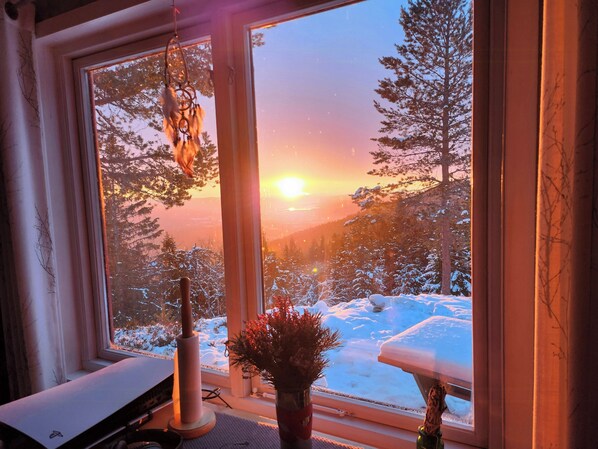 Ein Zimmer mit großem Fenster, Schreibtisch und Blumen in einer Vase.