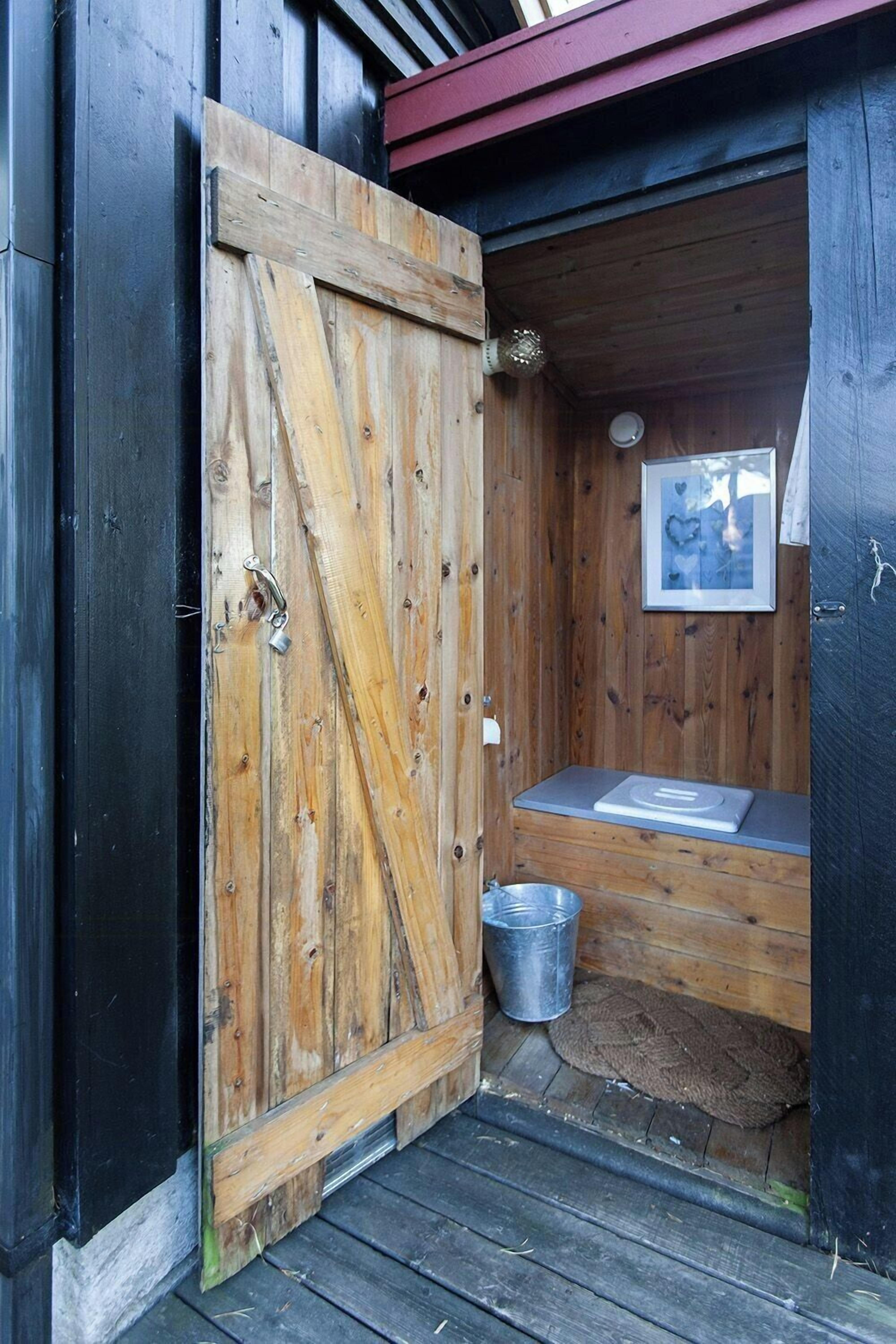 Eine rustikale Holztür, die zu einem kleinen, abgeschlossenen Raum mit einer Bank und einem gerahmten Bild an der Wand führt.