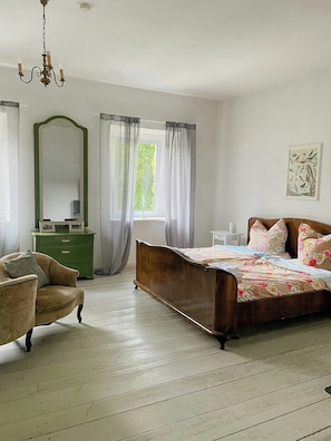 Un dormitorio con cama de madera, cómoda verde, una silla, un espejo y una ventana con cortinas.