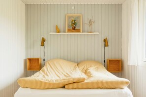 A bed with striped bedding, a framed picture on a shelf, and two wall-mounted lamps. - Nordic 70s gem amidst the dunes (Blokhus)