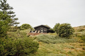 A cabin with a deck, surrounded by dense vegetation. - Nordic 70s gem amidst the dunes (Blokhus)