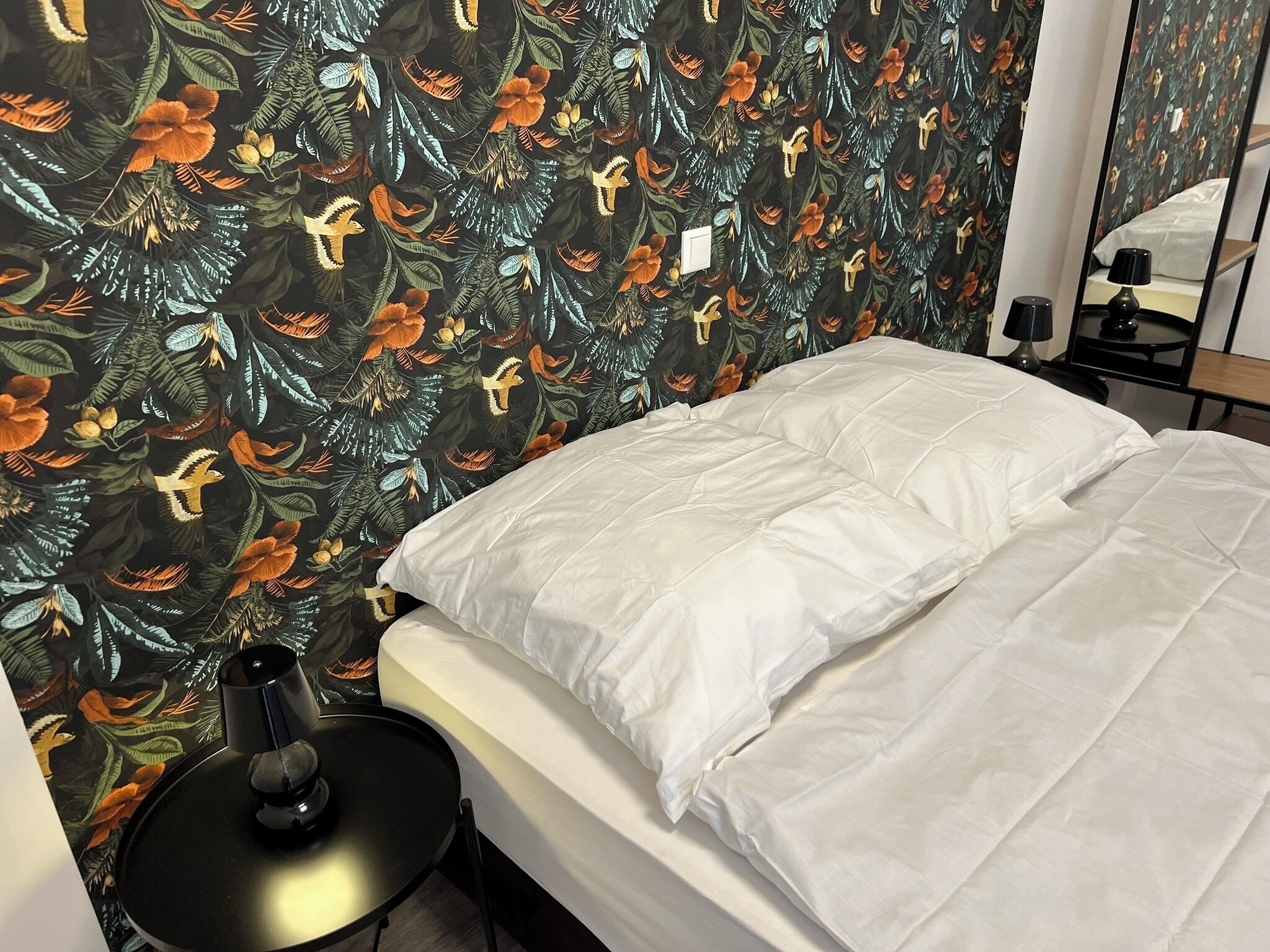 A hotel room with a bed, a small table, a lamp, and a mirror.