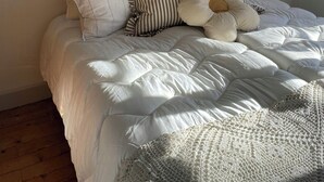 Una cama con un tapiz de macramé en la pared, un espejo redondo y una lámpara fijada a la pared.