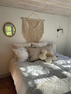 Ein Bett mit Wandbehängen aus Makramee, einem runden Spiegel und einer Wandleuchte.