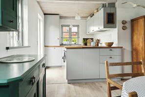 A kitchen with white cabinets, a wooden chair, and a window with a view of greenery. - Home with views and walking distance to nature (Nyborg)
