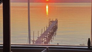 Ein Sonnenuntergangblick vom Fenster auf einen Steg, der sich in ruhiges Wasser erstreckt.