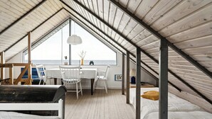 Ein Schlafzimmer im Dachgeschoss mit Holzbalkendecke, einem Esstisch, weißen Stühlen, einem Bett und Meerblick.
