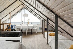 An attic bedroom with a wooden ceiling, a dining table, white chairs, a bed, and a view of the sea. - Home with views and walking distance to nature (Nyborg)