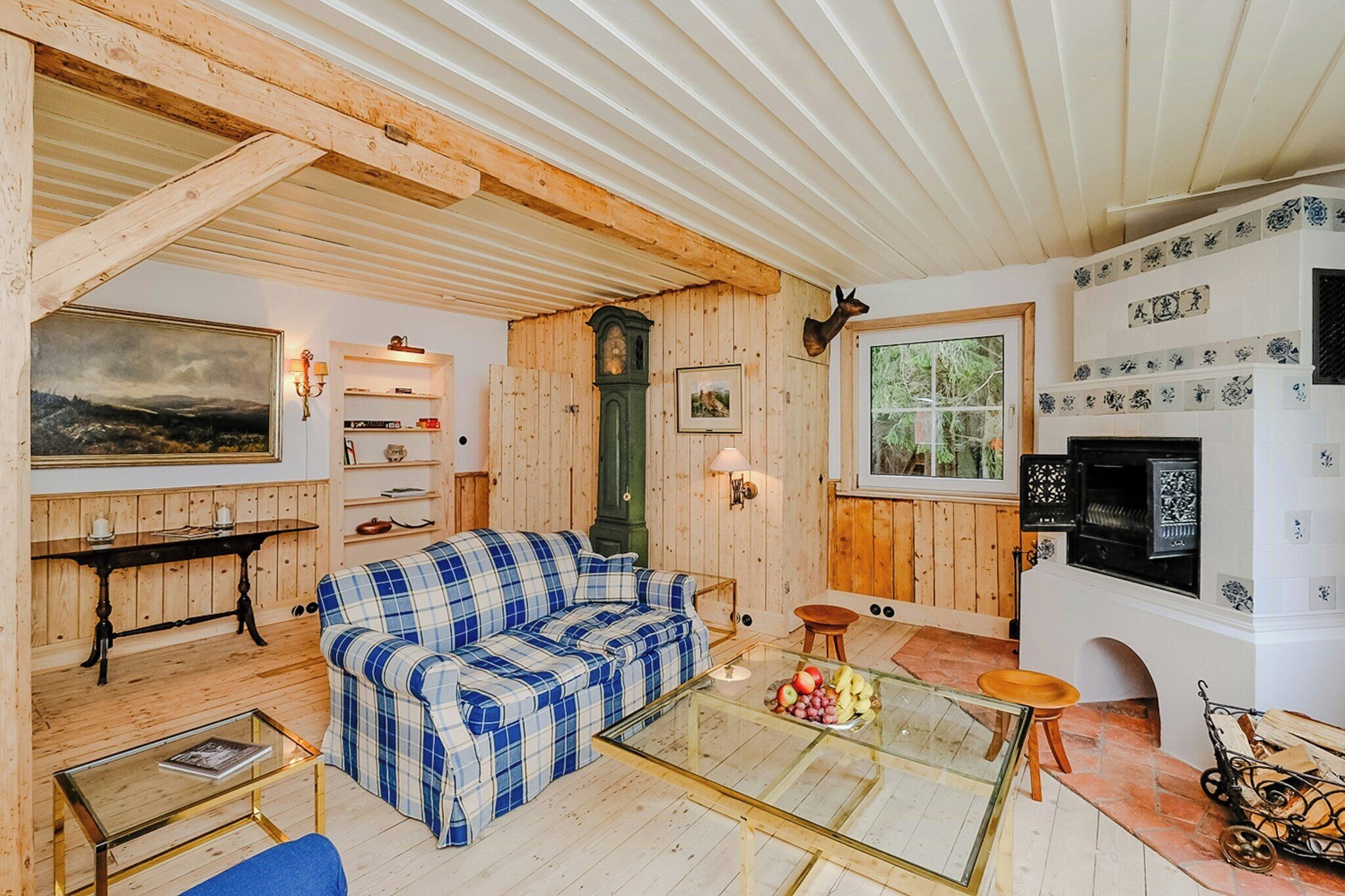Una habitación acogedora con un sofá de cuadros, una mesa de centro de vidrio, techo de madera, chimenea y un reloj.