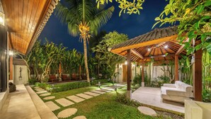 Uma área externa bem iluminada com pérgola de madeira, caminhos de pedra e vegetação exuberante.