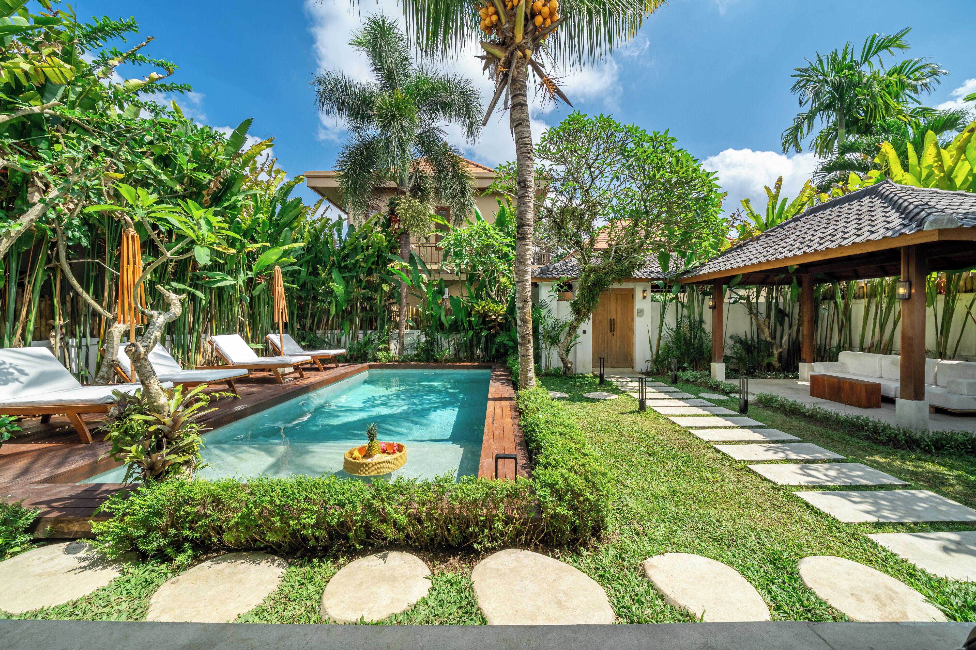 Una piscina rodeada de sillas de descanso, una terraza de madera y plantas tropicales.