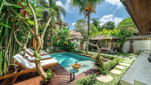 Uma piscina com espreguiçadeiras, um jardim com pedras no caminho e um gazebo.