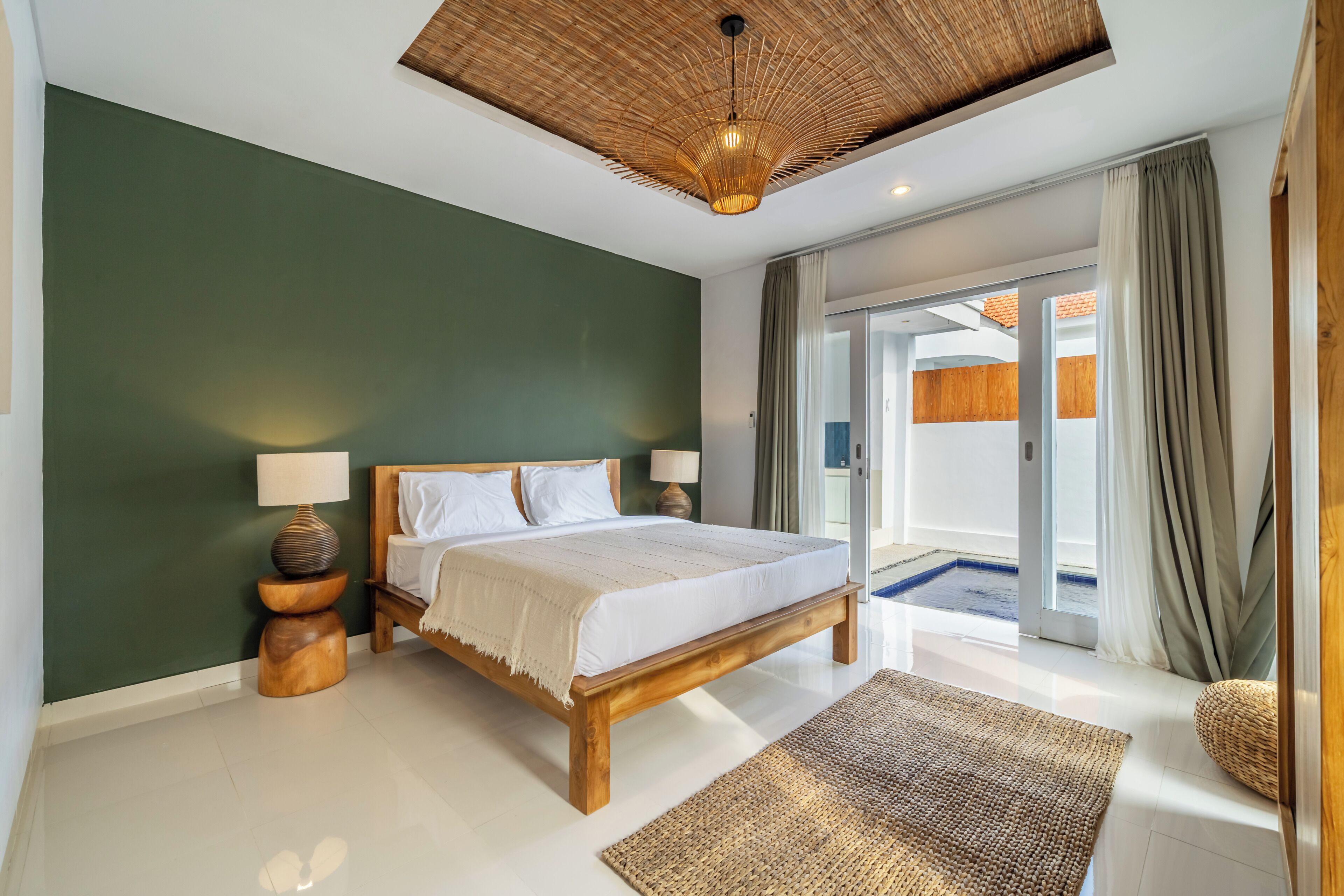 A bedroom with a bed, bedside lamps, a woven rug, and a view of a pool through a glass door.
