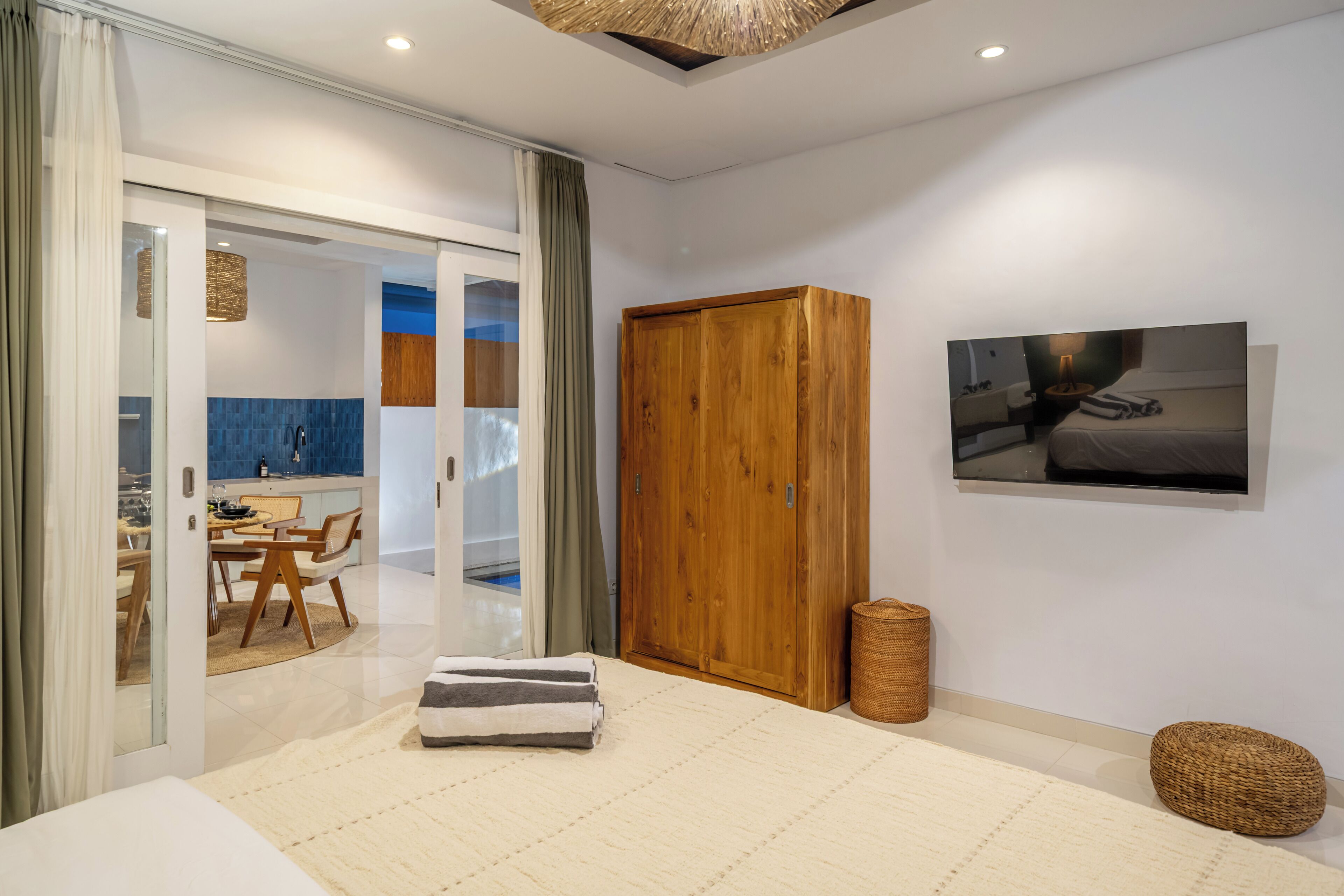 A modern bedroom with a large bed, a wooden wardrobe, a dining area with a view, and a bathroom with a blue-tiled wall.