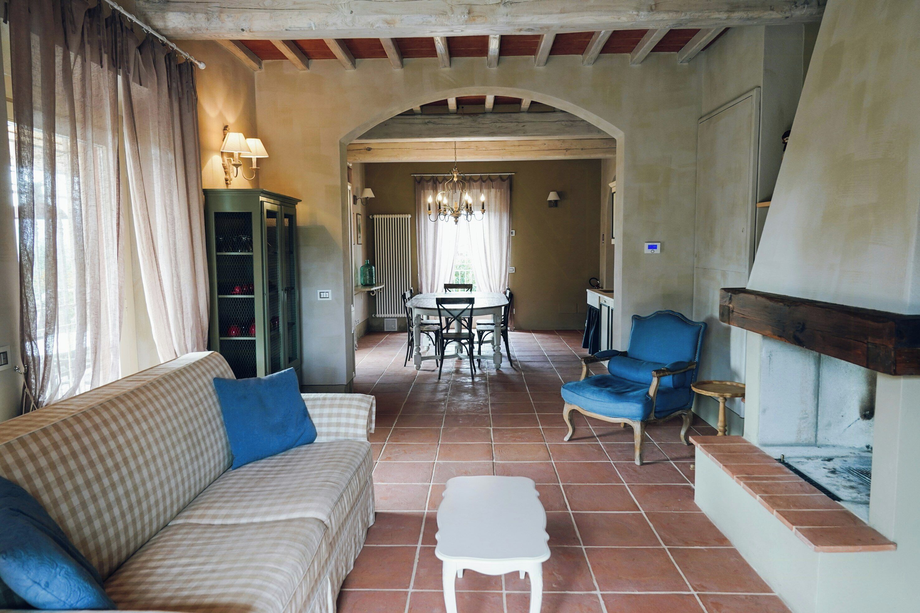 Un salon comprenant un canapé, une petite table, une table à manger avec des chaises, un fauteuil bleu et une cheminée.