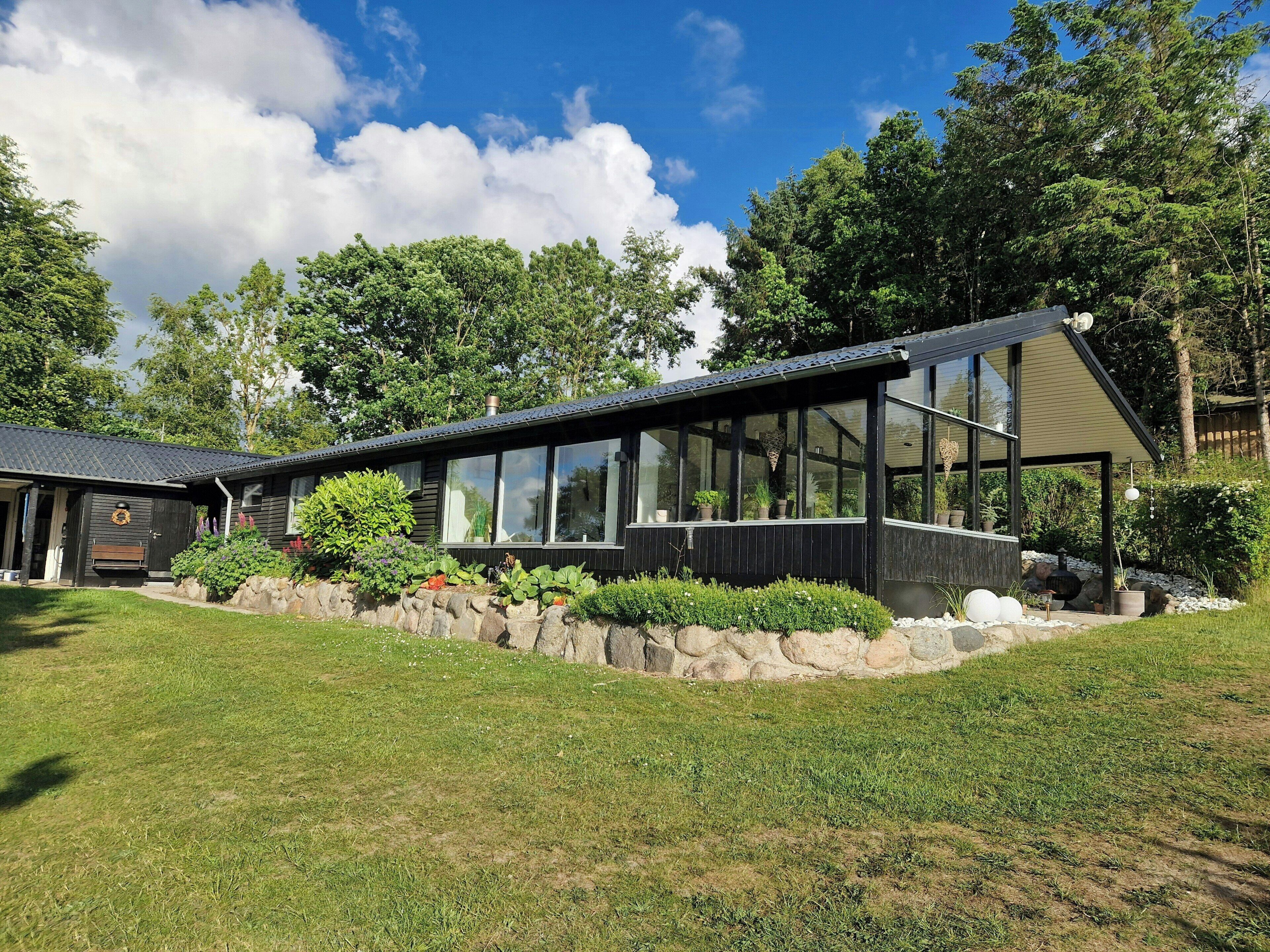 A modern house with a large glass window, a stone wall, and a grassy yard.