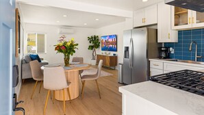 A modern kitchen with a stainless steel refrigerator, a built-in oven, and a gas stove. There is a dining area with a round table and chairs, and a sofa in the background. - Stylish North Park Escape - Private Patio (San Diego)