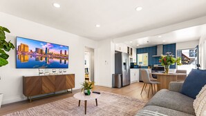 A modern living room with a flat-screen TV, a sofa, a coffee table, and a kitchen in the background. - Stylish North Park Escape - Private Patio (San Diego)