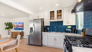 A modern kitchen with white cabinets, a stainless steel refrigerator, a gas stove, and a blue tiled backsplash. - Stylish North Park Escape - Private Patio (San Diego)