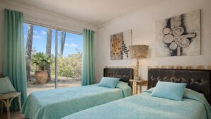 Ein Zimmer mit zwei Betten, einem Fenster mit Vorhängen, einer Zimmerpflanze und Bildern an der Wand.