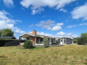 Une maison moderne dotée d’un patio couvert, d’une cheminée en briques et d’une pelouse bien entretenue.