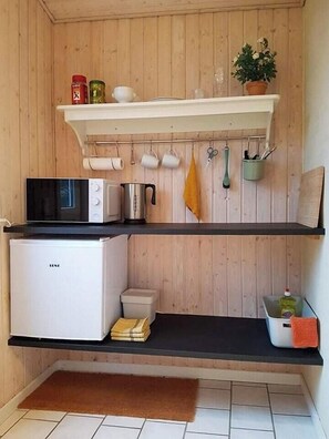 Eine kleine Küche mit Mikrowelle, einem Kühlschrank, einem Regal mit Küchenutensilien und einem Topf mit Pflanze.