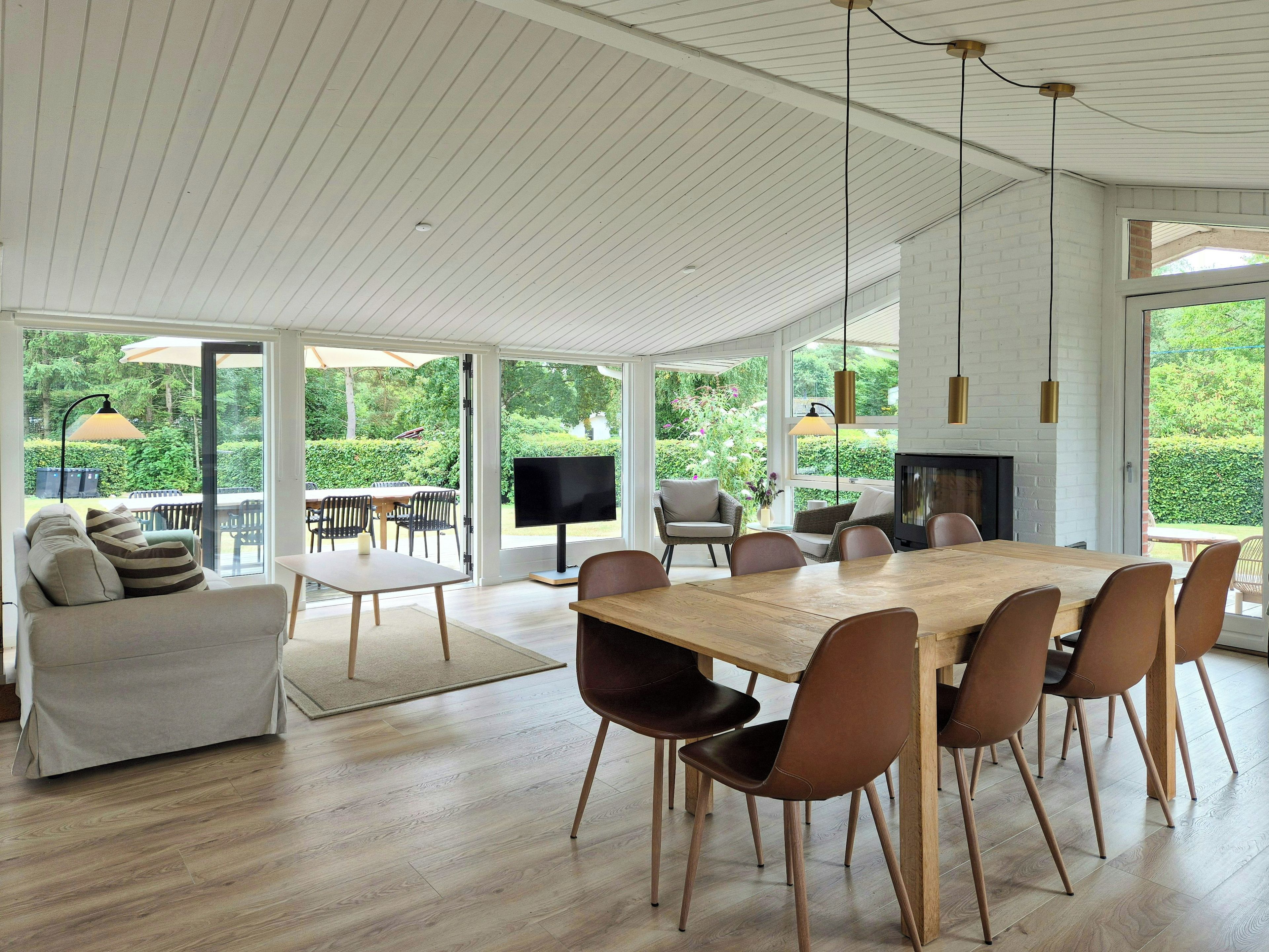 A spacious dining area with a large wooden table and modern chairs, a cozy seating area with a sofa and armchairs, and a television on a stand.